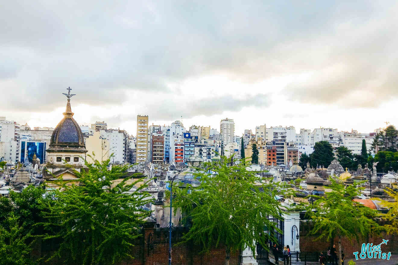 A cityscape view of Buenos Aires, displaying an array of tombs and mausoleums in the foreground at Recoleta Cemetery, with modern apartment buildings rising in the background