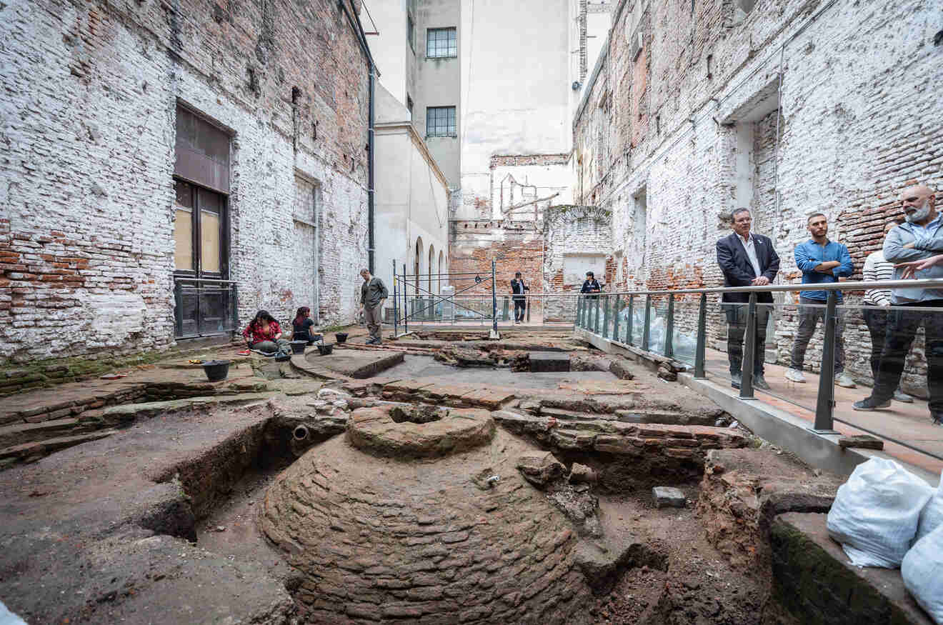 People exploring at a historical excavation site within a rustic urban courtyard at Manzana de las Luces, surrounded by the weathered walls of an old Buenos Aires building