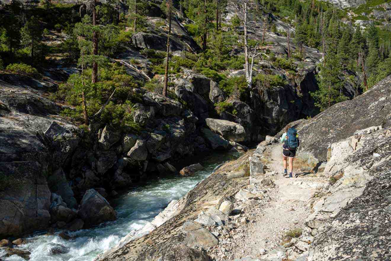 A hiker is walking down a rocky trail next to a river.