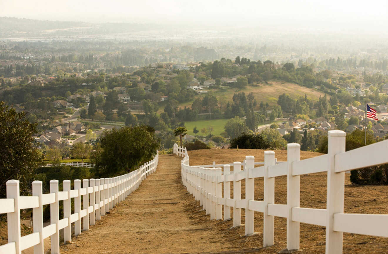 a path with white fence leading downhill with view of the city in the bakcground