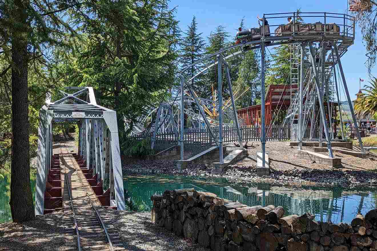 A wooden roller coaster in a park with trees.