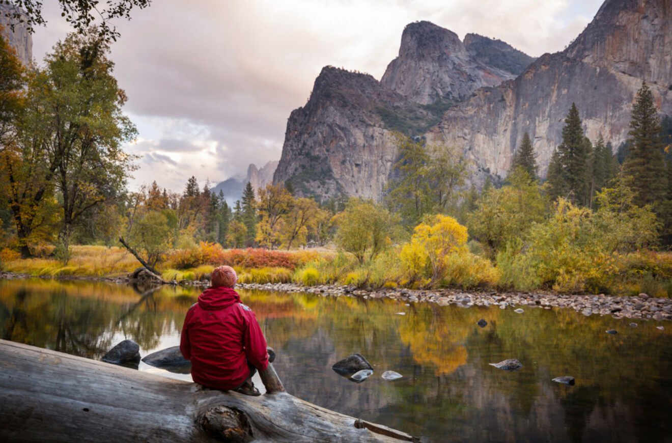 a person sitting on a rock next to a lake with rocky mountains in the background in fall (autumn)