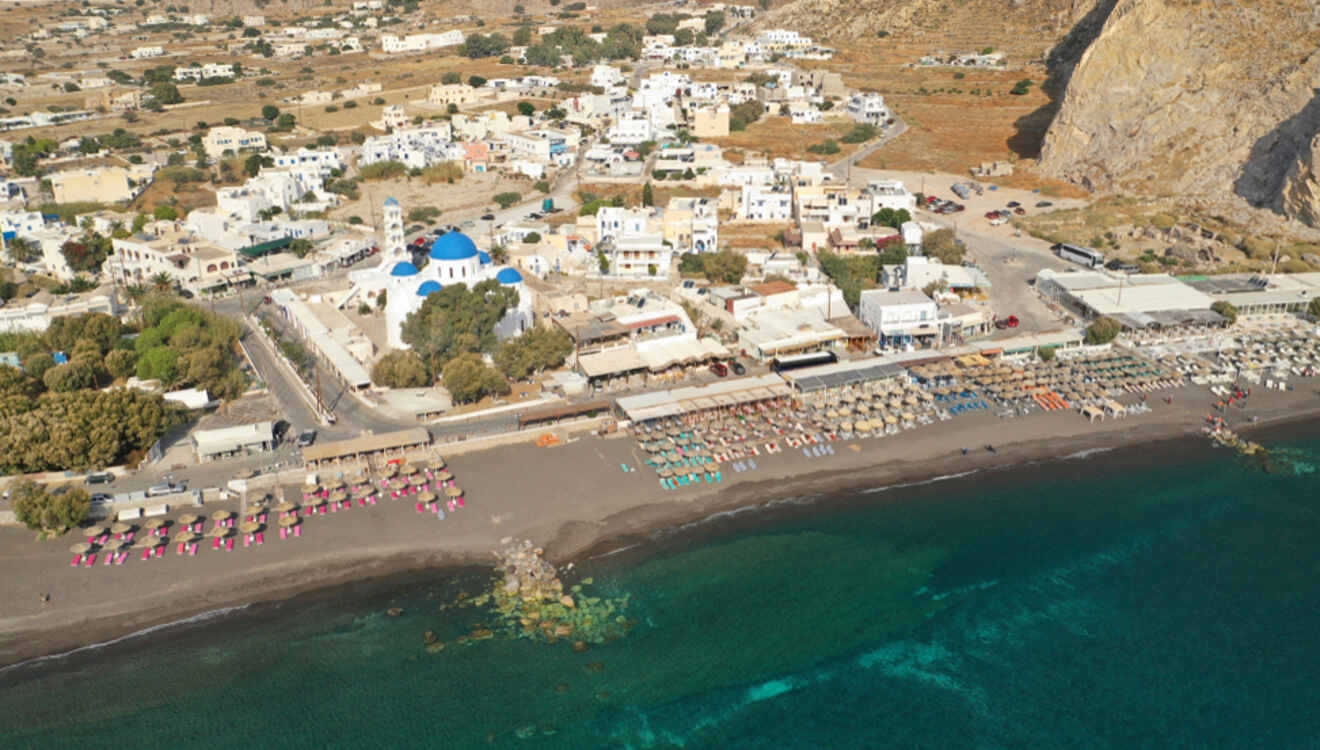 Aerial view of a Santorini beach lined with colorful umbrellas and a blue-domed church