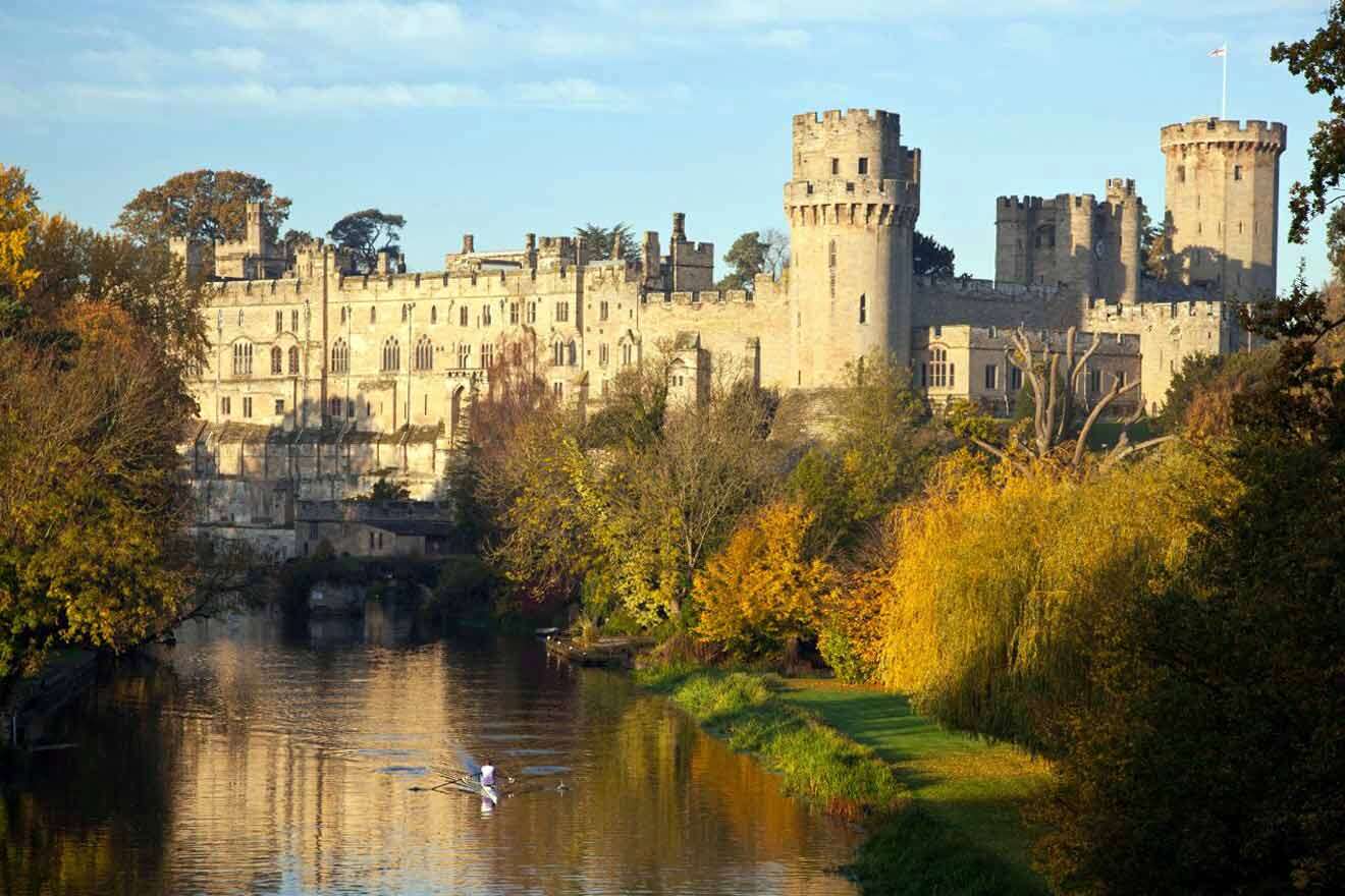 A man is rowing down a river with a castle in the background.