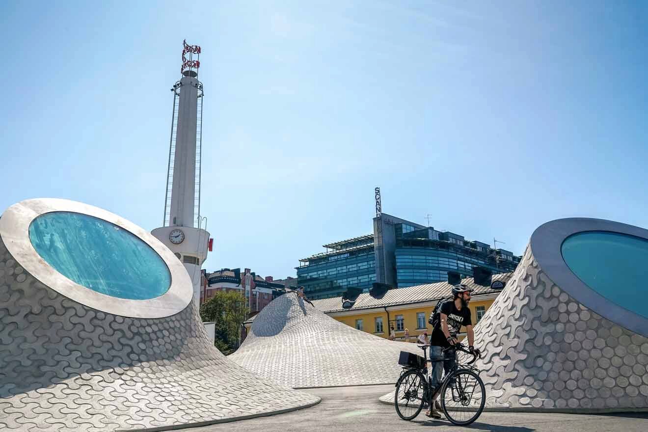 A man riding a bicycle in front of a sculpture.