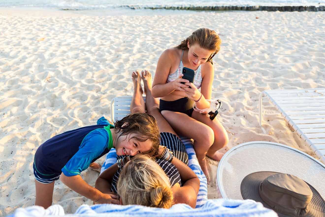 A mom with her kids sitting on a beach in the Cayman Islands with a cell phone.