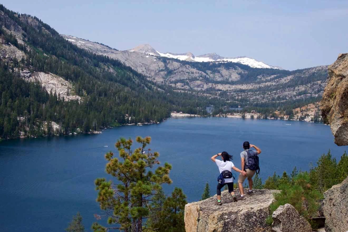 Two people standing on a cliff overlooking a lake.