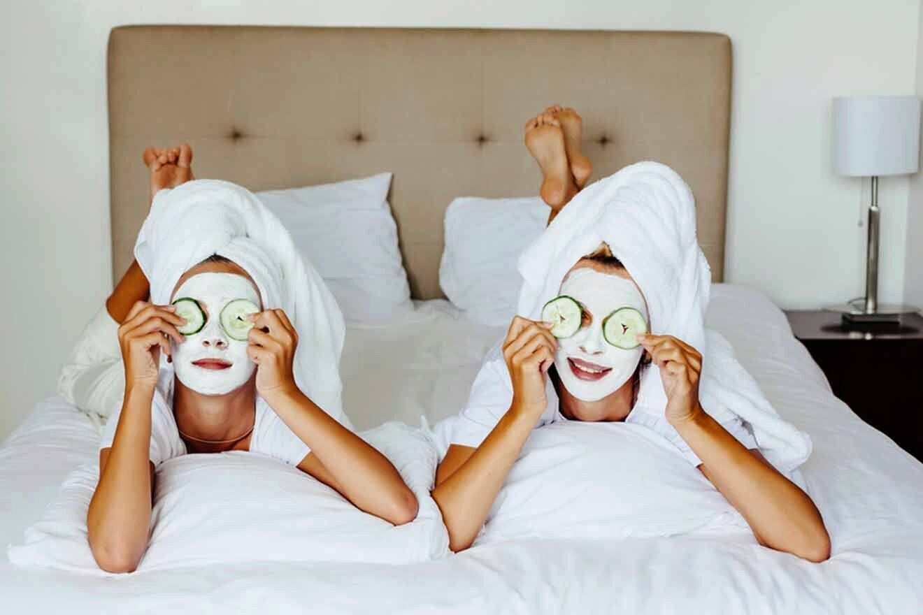 Two women laying on a bed with cucumber masks on their faces.