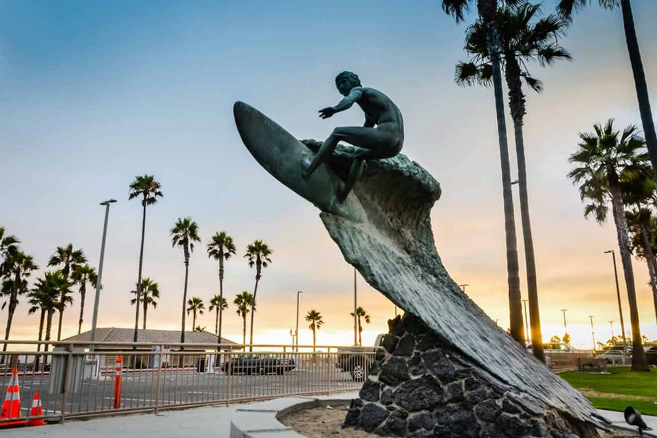 A statue of a surfer riding a wave in front of palm trees.