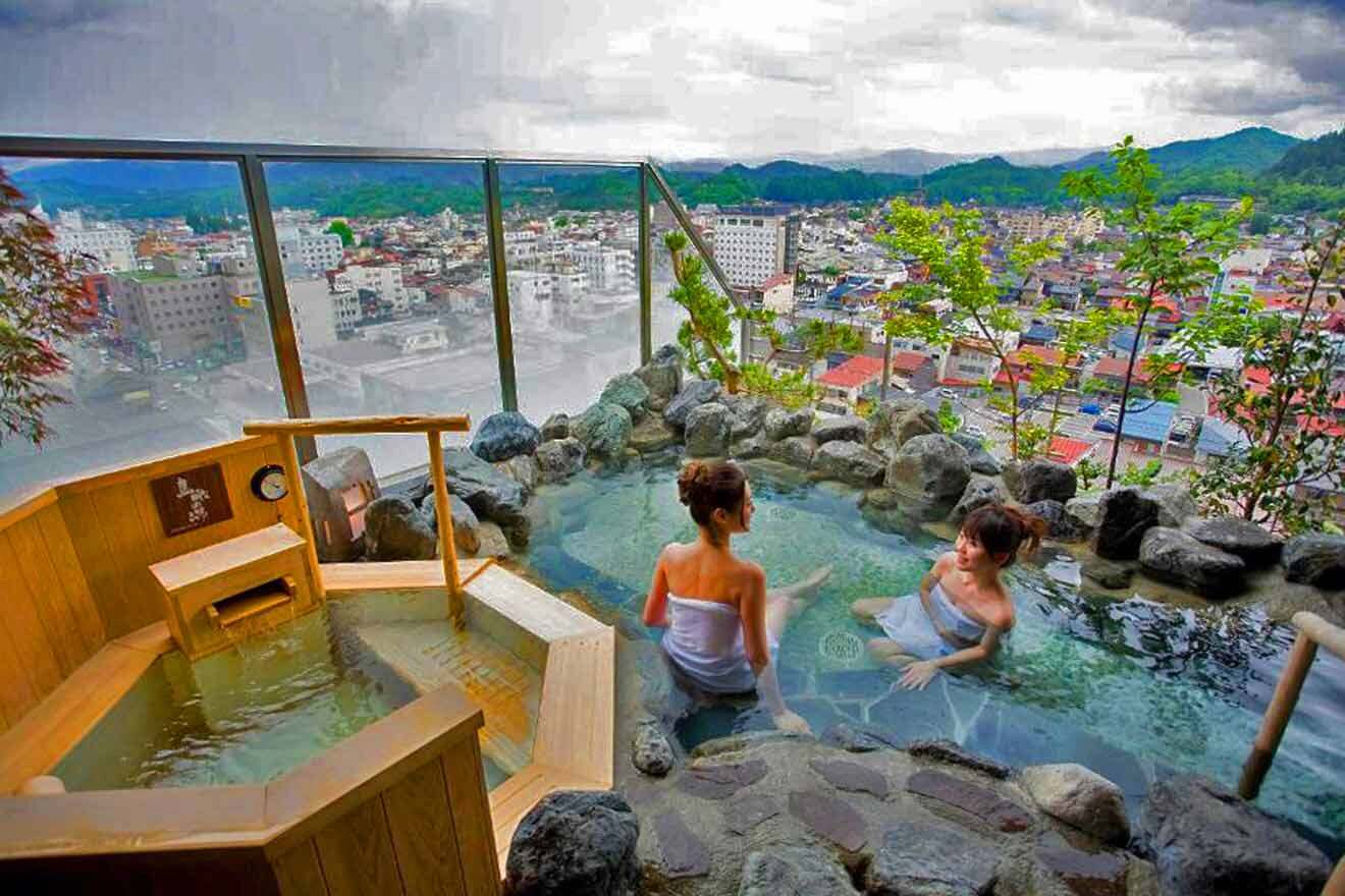 Two women sitting in a private onsen overlooking a city.