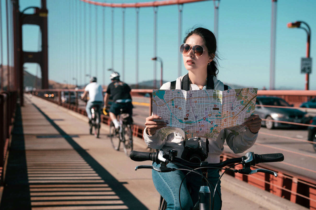 A woman on a bike holding a map over the golden gate bridge.