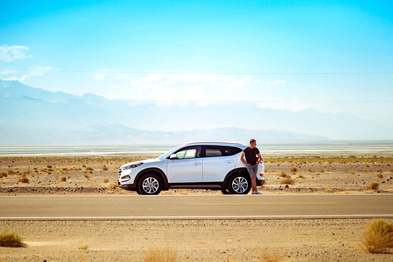 A man standing next to a white suv in the desert.