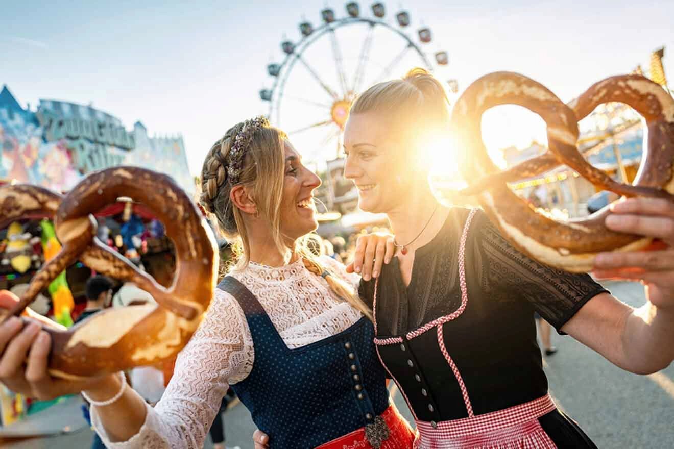 Two women holding pretzels in front of a ferris wheel at oktoberfest