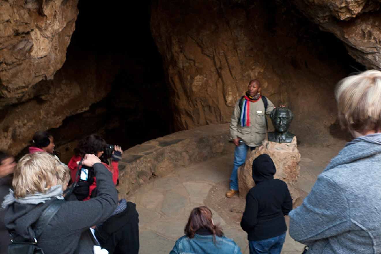 A tour guide speaks to a group of people inside a cave next to a bust statue.