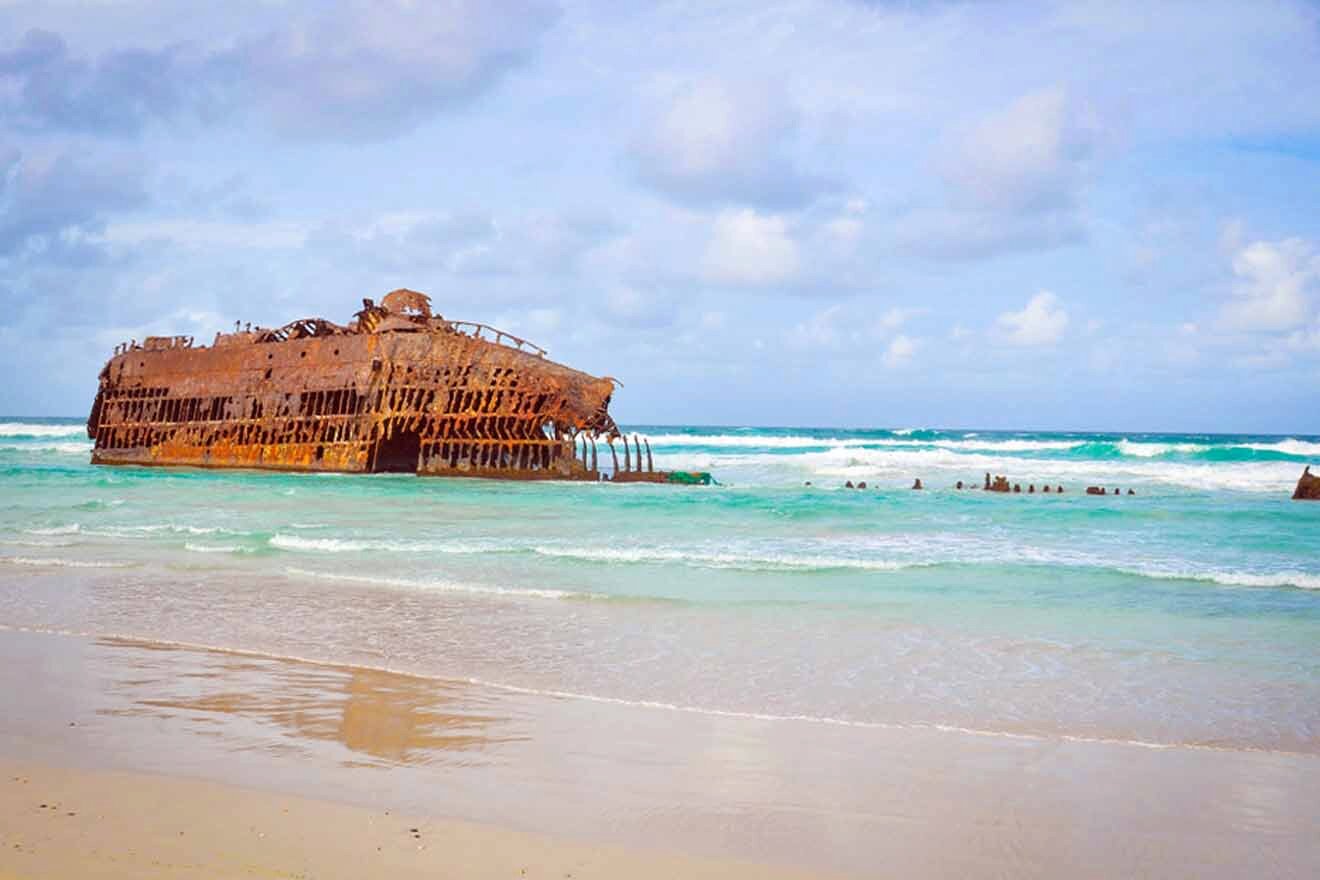 A rusty ship sits on a beach near the ocean.