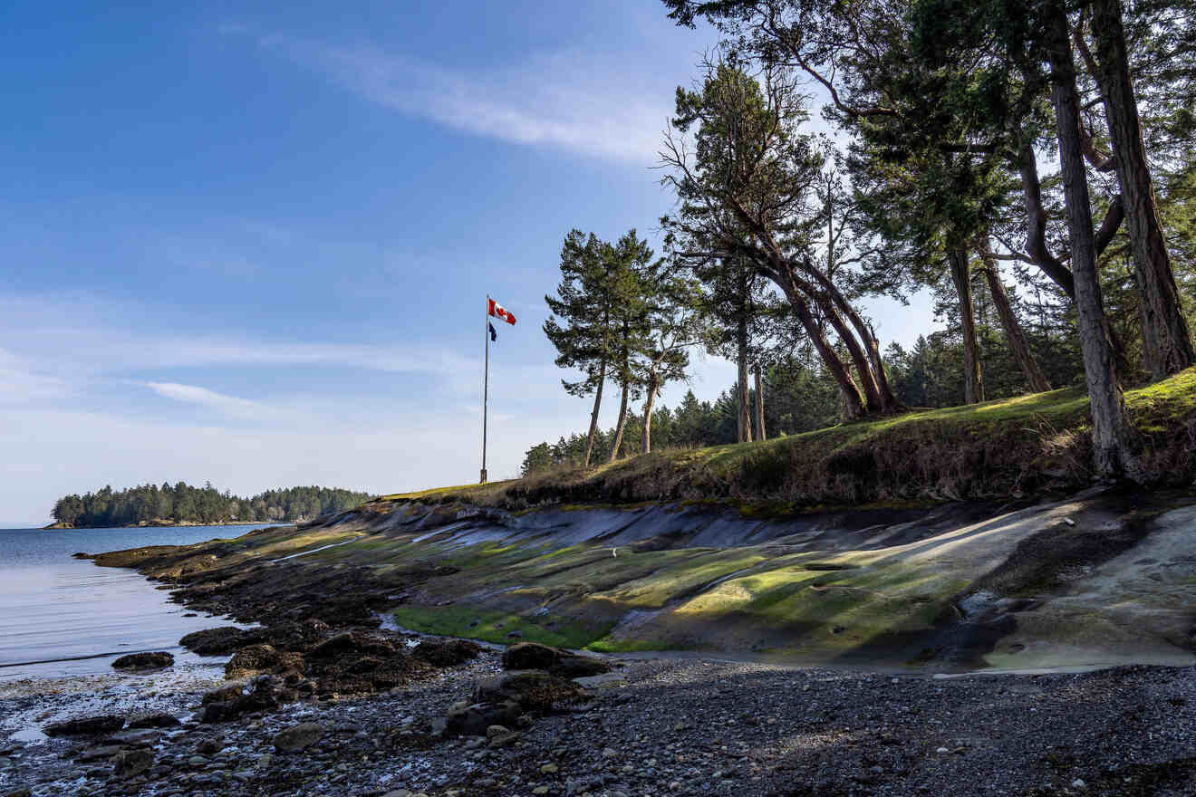 A canadian flag is flying over a rocky shoreline.