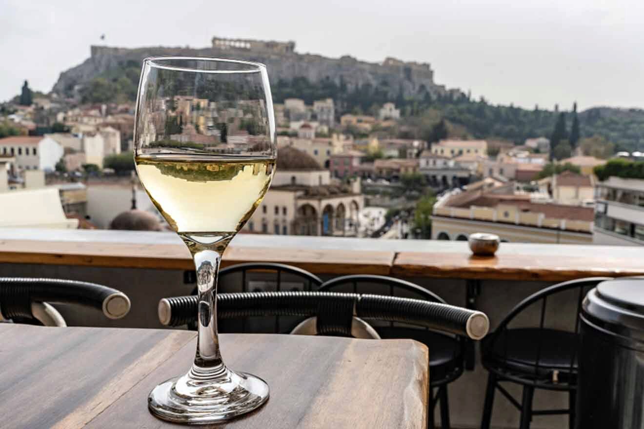 A glass of white wine on a table with a view of the acropolis.