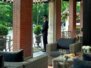 A man is standing in front of a patio with wicker furniture.