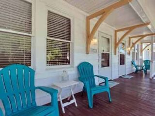 A porch with blue adirondack chairs on it.
