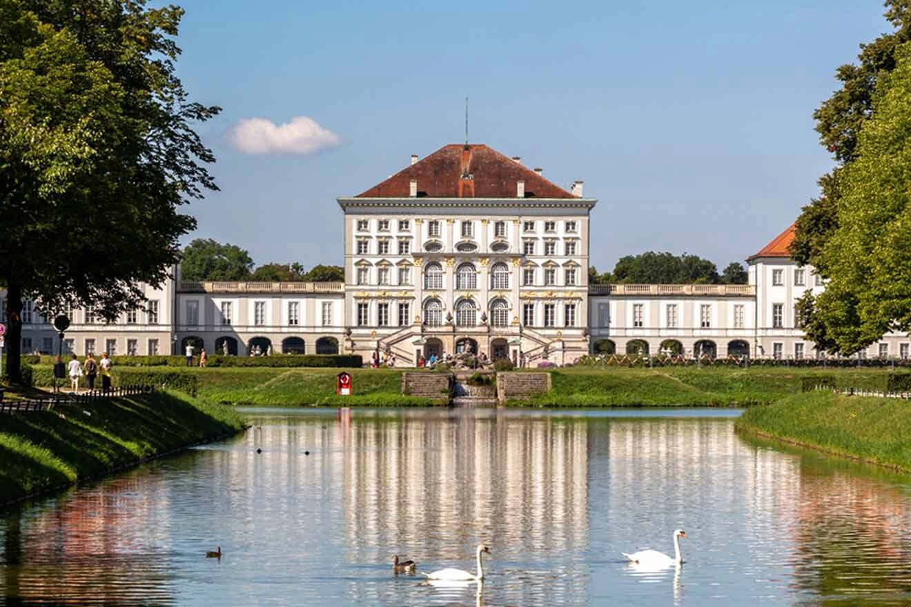 Two swans swimming in a lake in front of a large building.