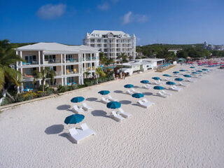 view of hotel exterior and beach with lounge chairs and umbrellas