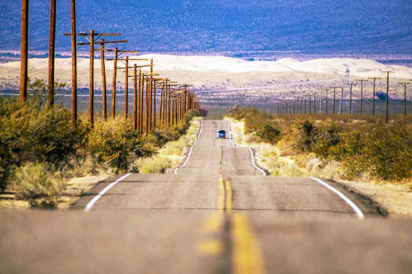 A car is driving down an empty road in the desert.