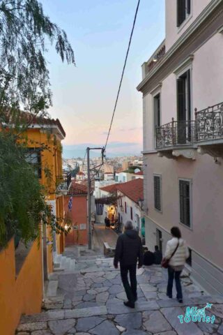 people walking down a steep stairway in the old town of athens.