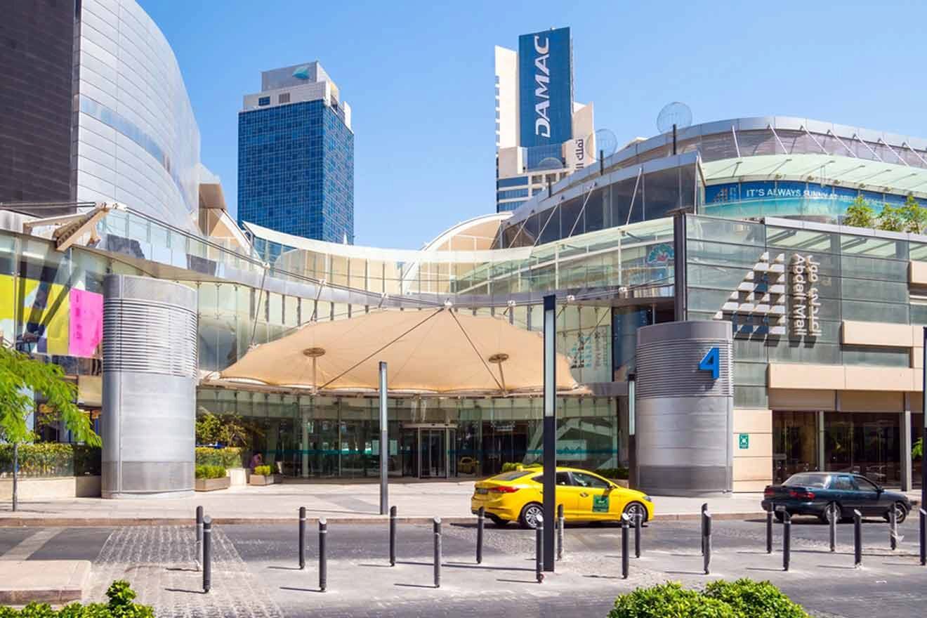 A shopping mall with a yellow car parked in front of it.