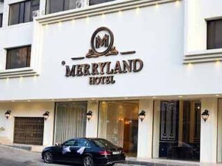 The merland hotel is a white building with a car parked in front of it.