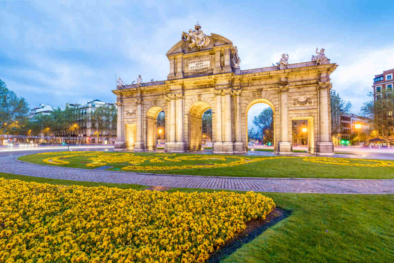 An arch in the middle of a city with yellow flowers.