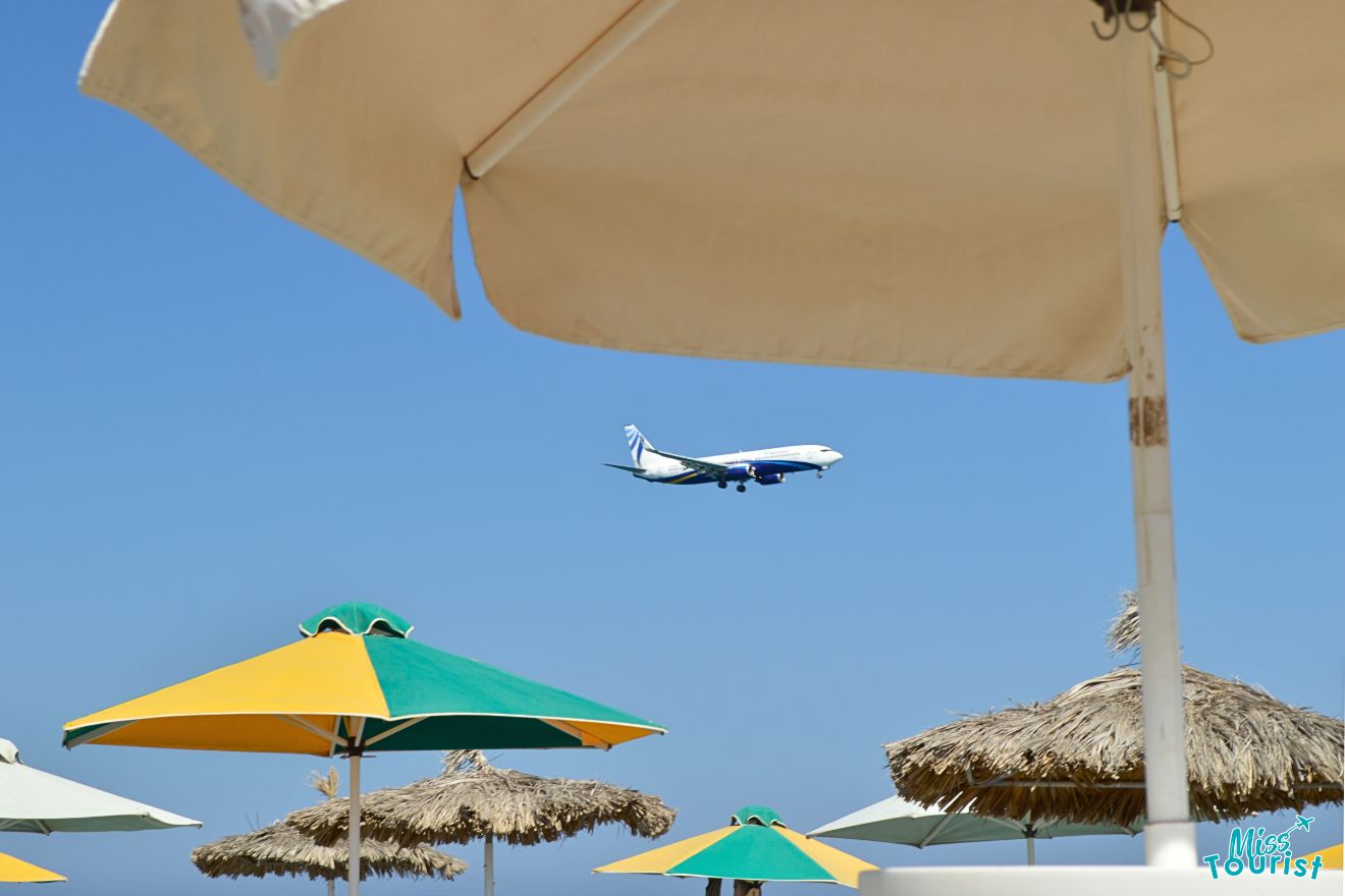 A plane flying over a beach with umbrellas.