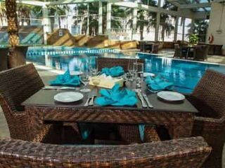 A table with wicker chairs and a pool in the background.