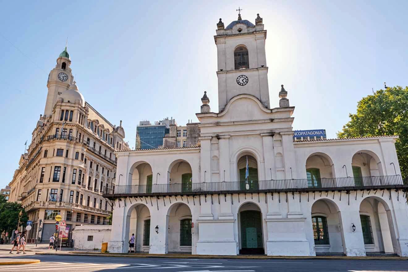 A white building with a clock tower in the middle of the street in Buenos Aires.