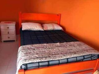 A bed in a room with orange walls and white nightstand.