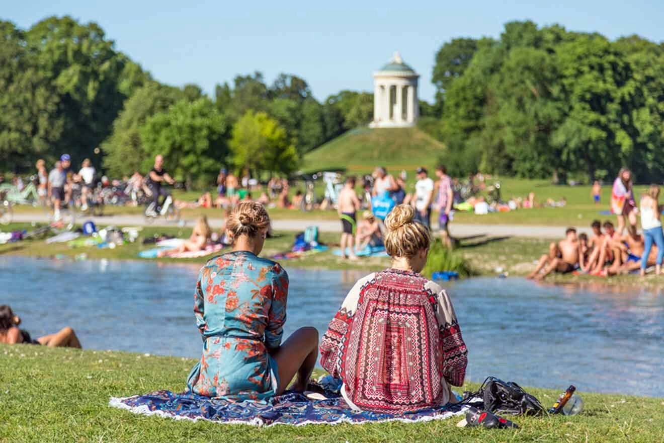 people sitting on the grass next to a river with 2 women in foreground