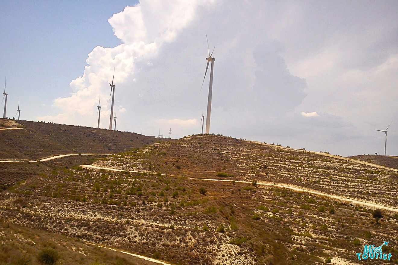 Wind turbines on a hillside with a cloudy sky.