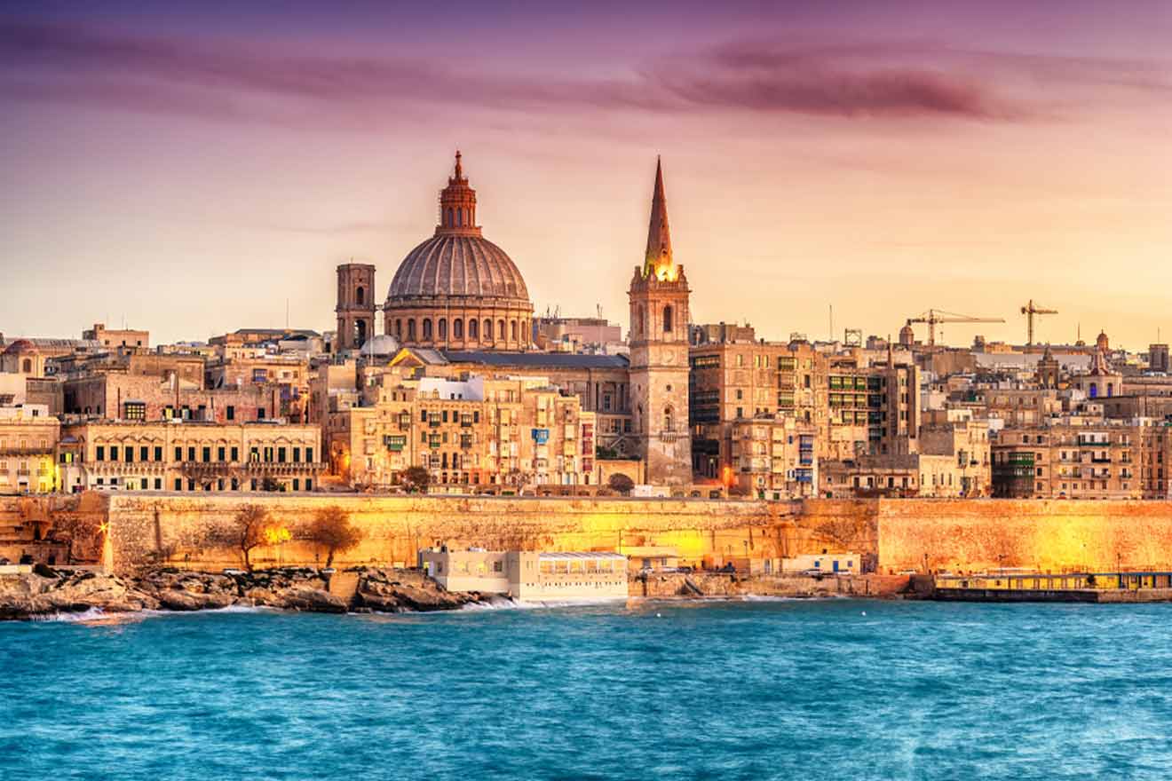 Sunset view of Valletta's skyline, featuring the iconic St. Paul's Cathedral dome and the city's ancient sandstone buildings, with the serene Mediterranean Sea in the foreground.