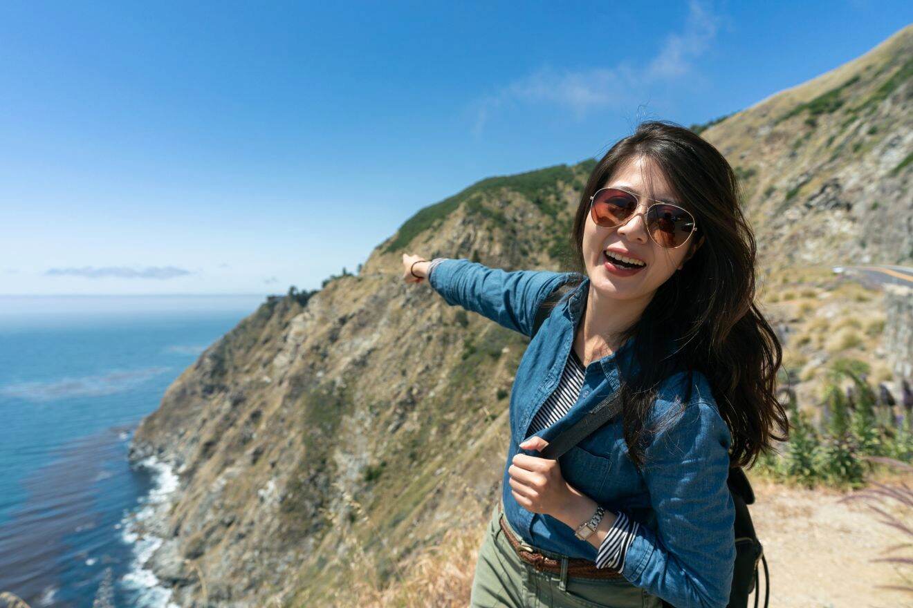 A woman is standing on a cliff overlooking the ocean.