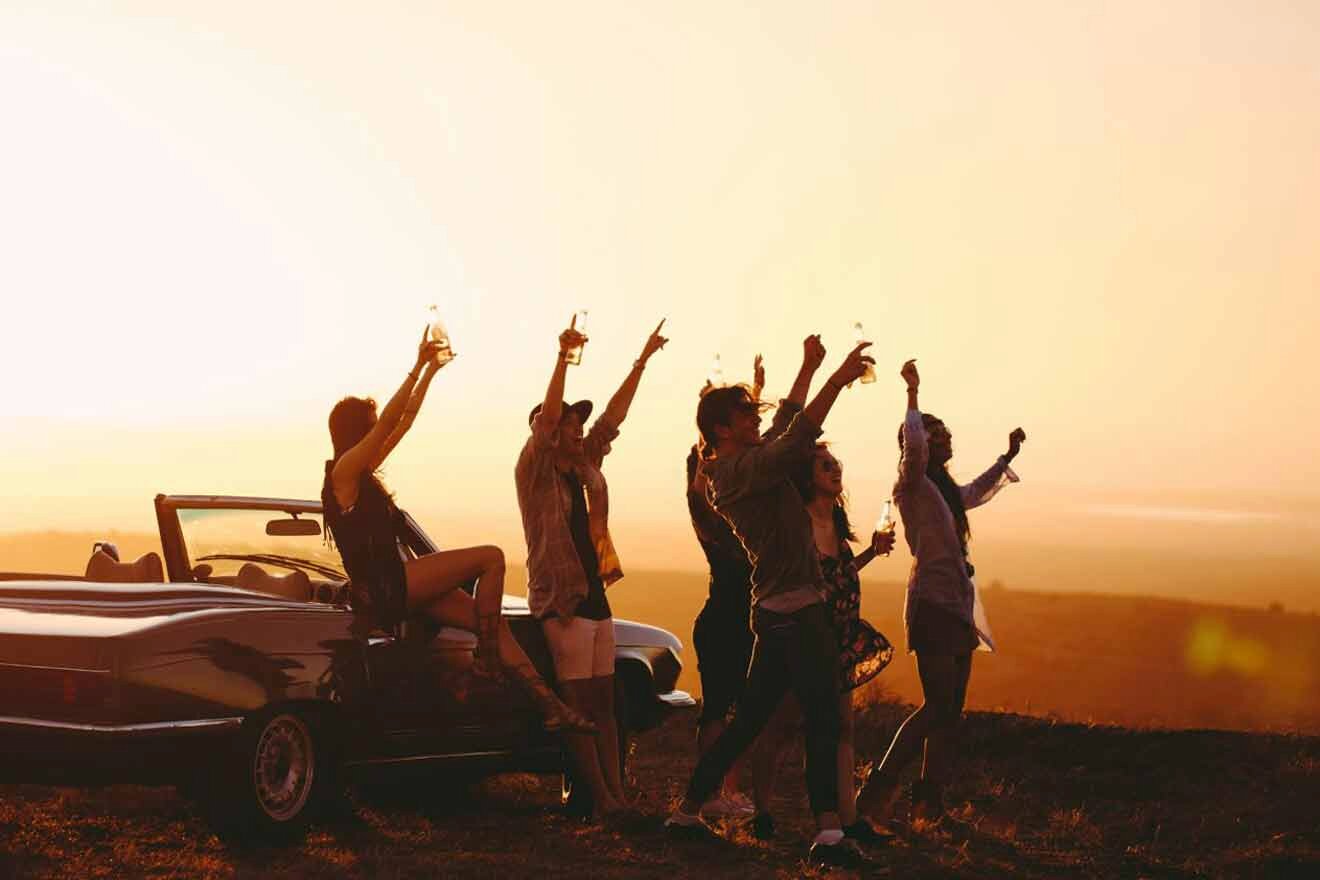 A group of people standing on a hill with a car in the background.