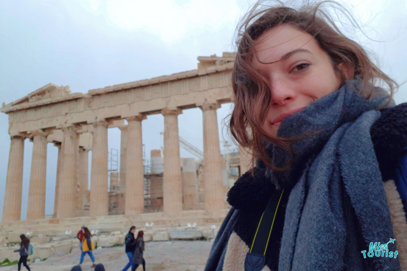 A woman wearing a scarf in front of the parthenon.