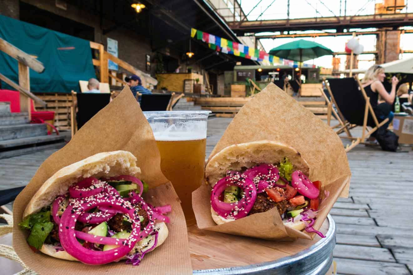 Two vegan sandwiches on a table next to a beer.