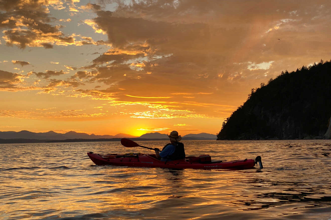 A person is paddling a kayak in the water at sunset.