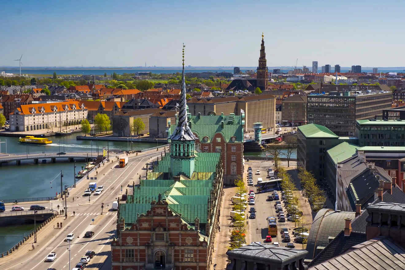 Panoramic view of Copenhagen's cityscape featuring historical buildings, a prominent spire, and bustling city streets with a clear blue sky in the background