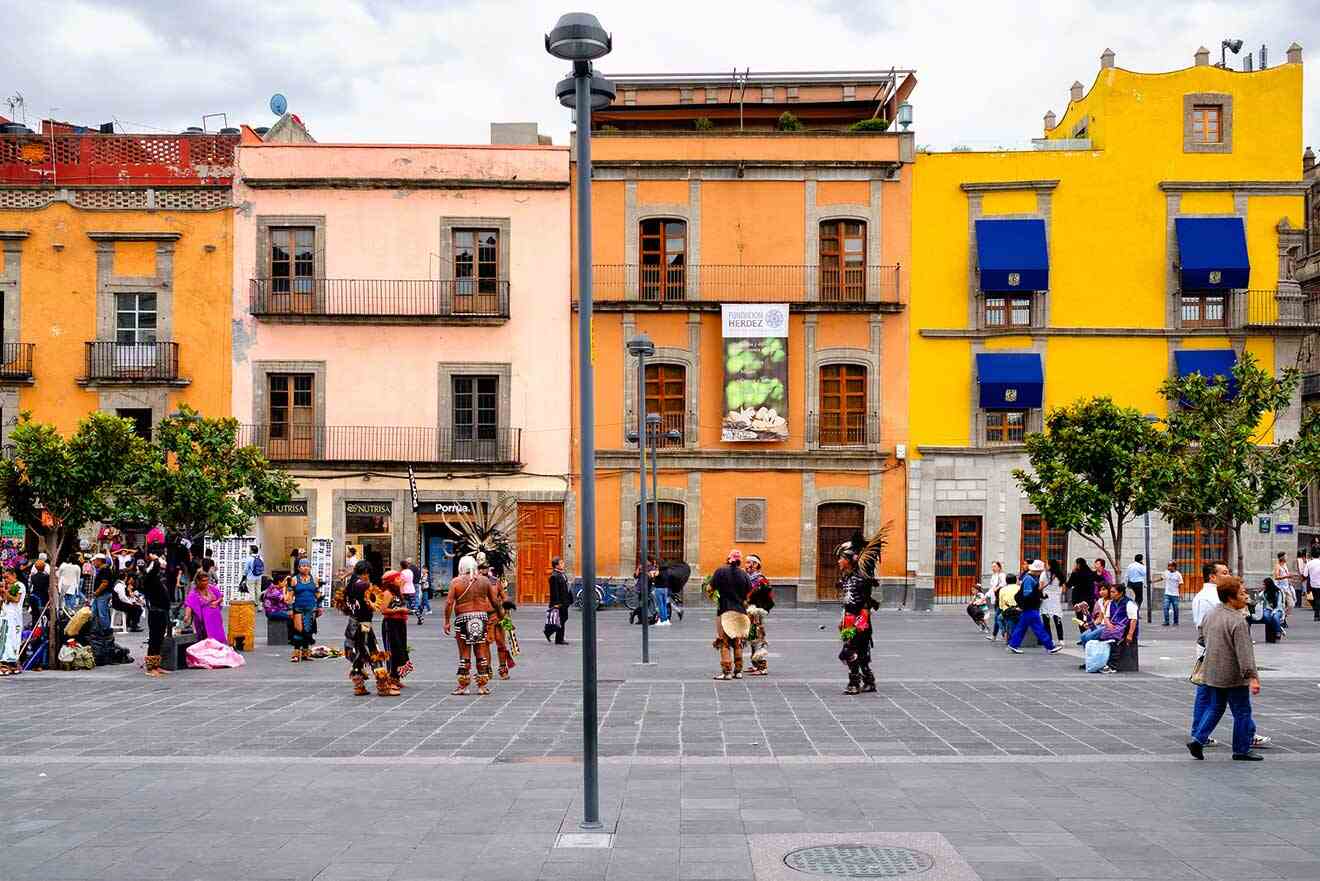 People are walking around a square with colorful buildings in Mexico City