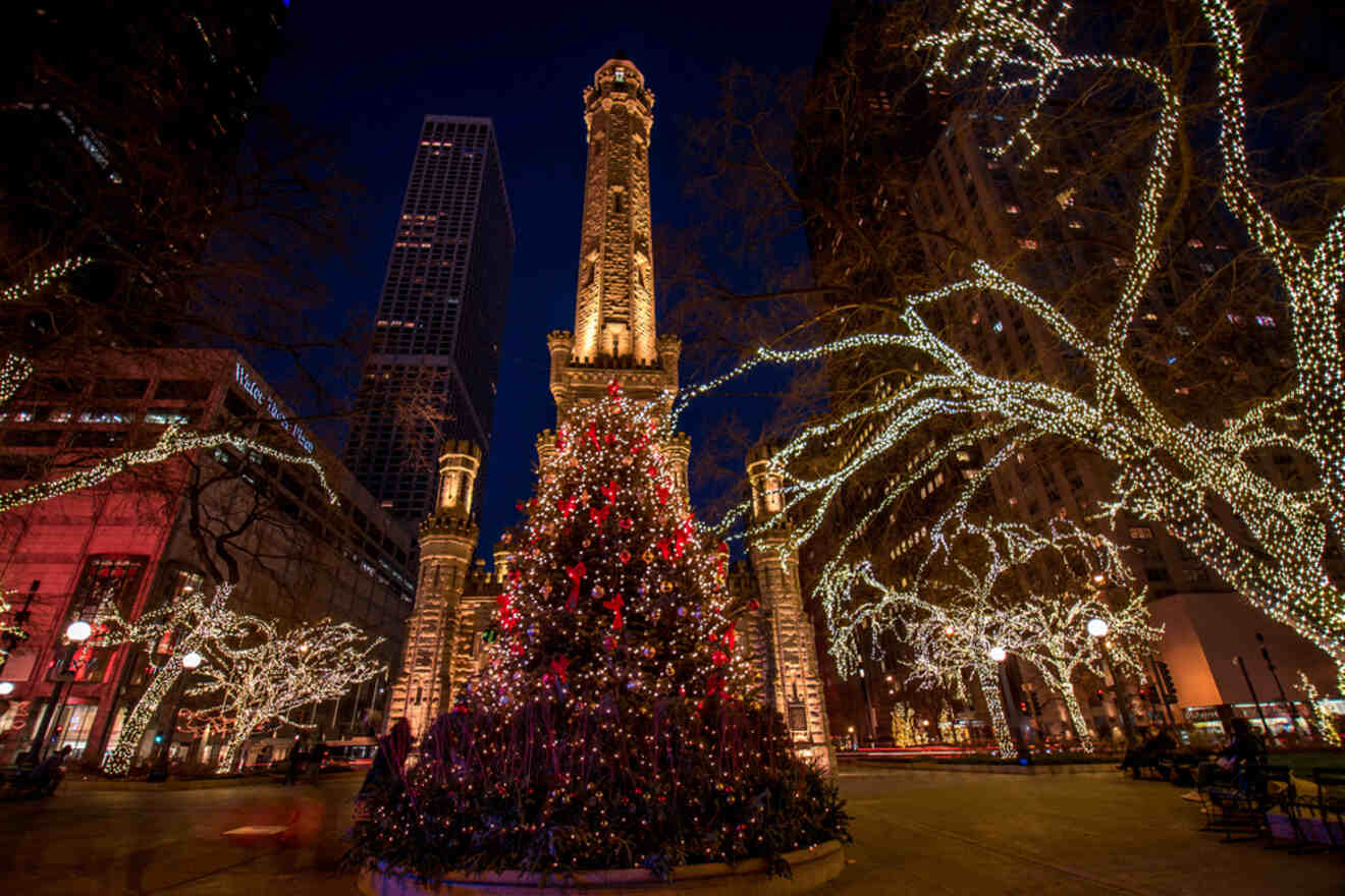 a Christmas tree in front of a tower surrounded by trees with twinkling lights