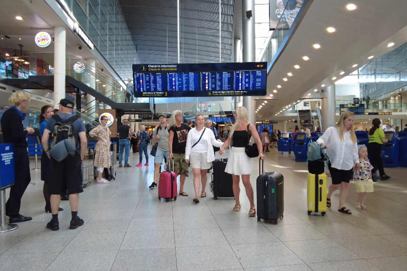 Bustling interior of Copenhagen Airport with travelers and flight information displays, capturing the lively atmosphere of a major travel hub