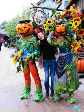 A woman is posing with two people dressed up as pumpkins in Disneyland Paris