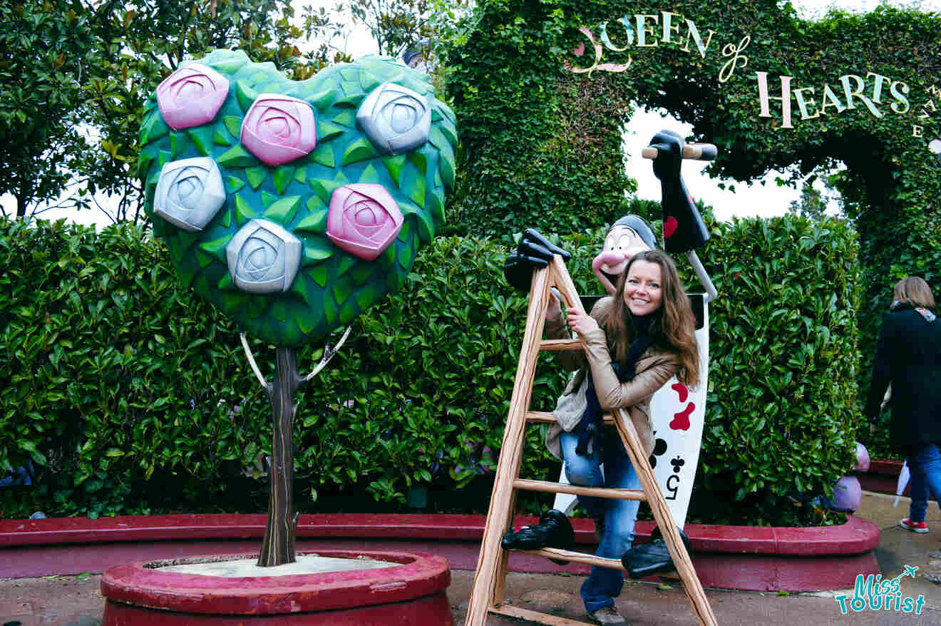 A girl standing next to a statue of a lady of hearts and a tree with roses in Disneyland Paris