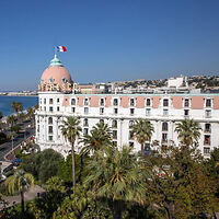 Historic luxury hotel facade with a distinctive pink dome, palm trees, and a view of the sea, embodying the elegance of seaside architecture.
