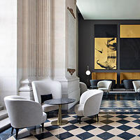 A luxurious hotel lounge with grey armchairs, a columned entrance, and a large abstract painting, set against a checkered floor